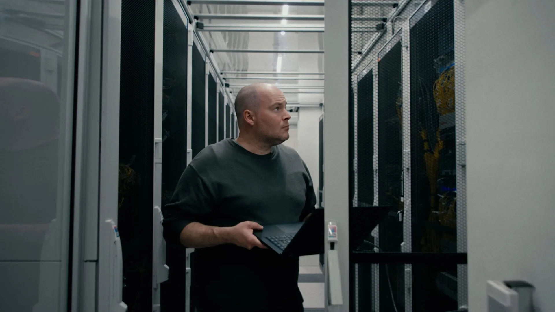 Ein Techniker steht mit Laptop im Gang eines Rechenzentrums und prüft ein Rack