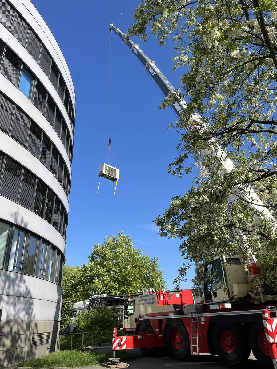 A mobile crane lifting an air conditioning unit off the roof of an office building